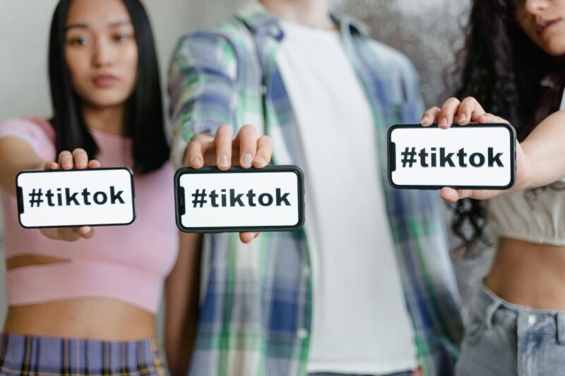 TikTok Shopを象徴するハッシュタグを表示したスマートフォンを若者たちが手に持っている様子