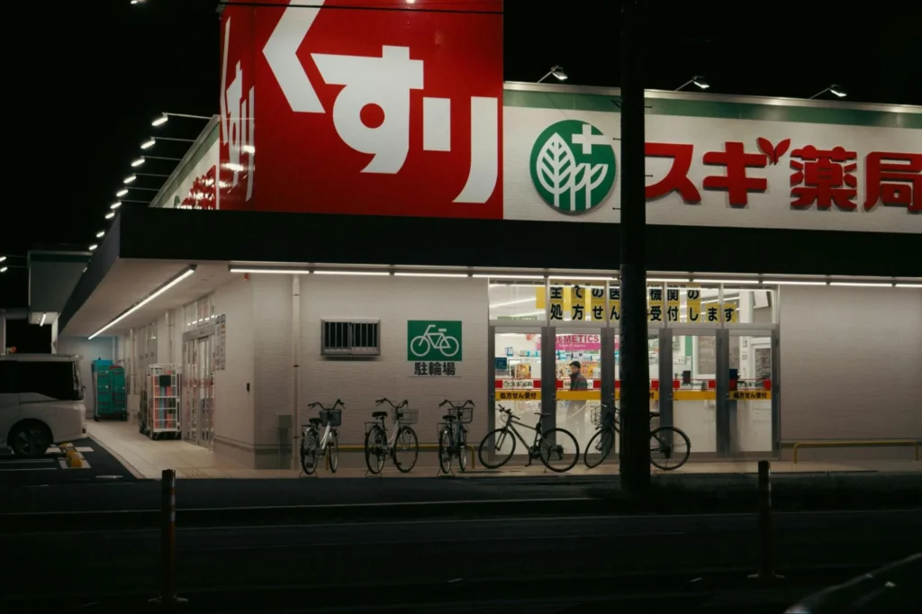 夜間にライトアップされたスギ薬局の店舗外観。「くすり」の大きな赤い看板と、駐輪場に並ぶ自転車。