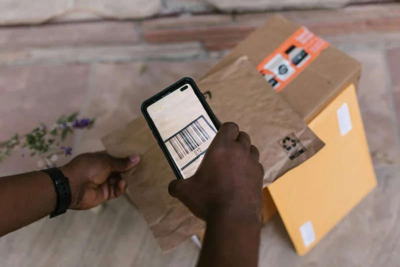 配達員がスマートフォンのカメラを使用して、Amazonの配送荷物にあるバーコードをスキャンしている手元の様子。